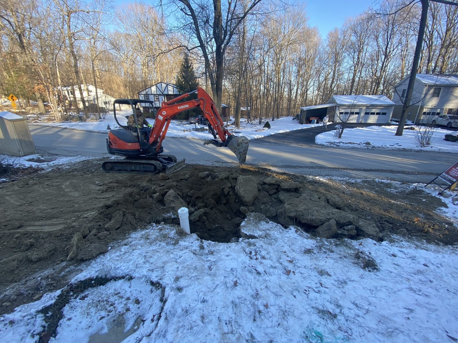 Our excavator digging a utility trench beside a house in the snow